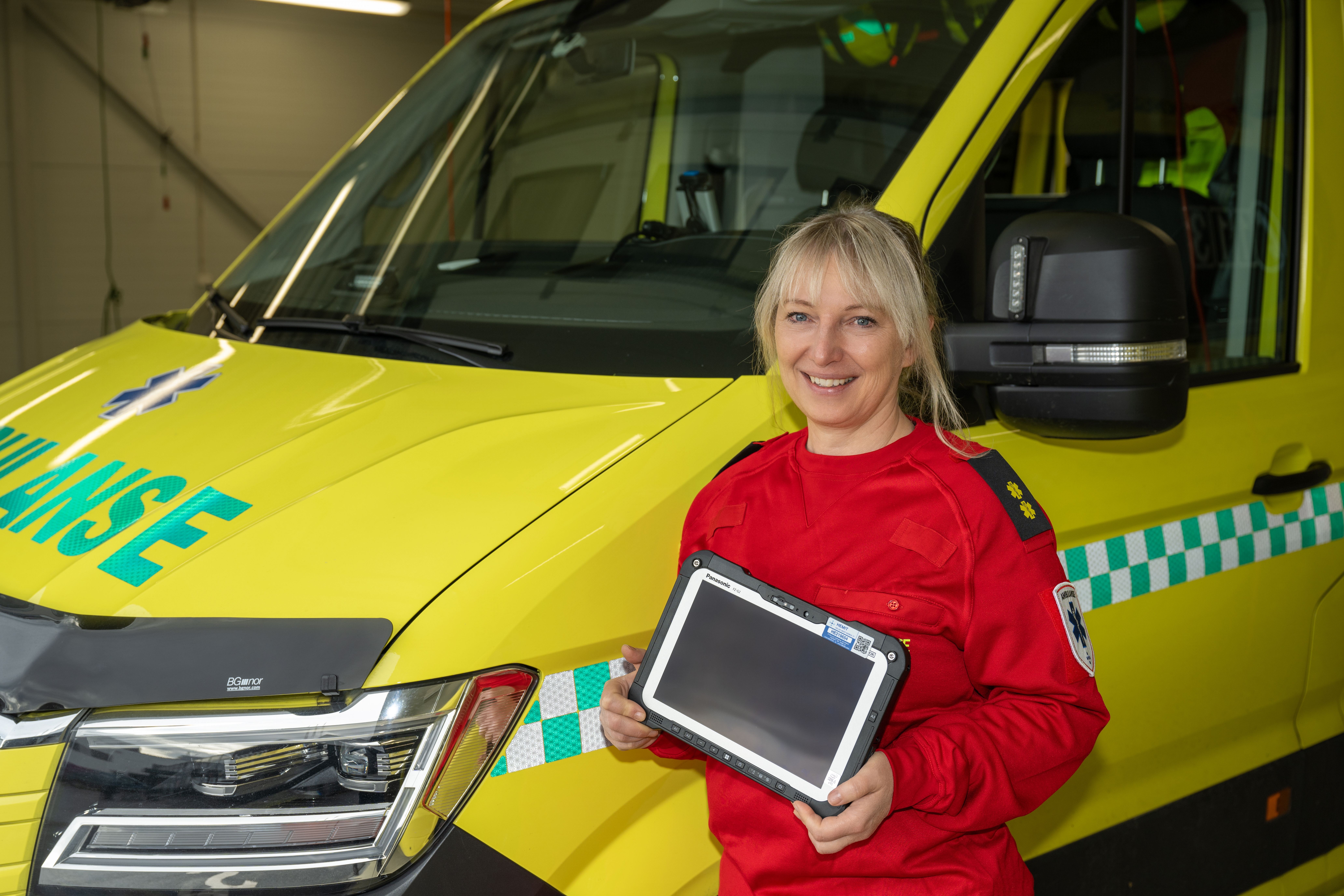 Ambulanseansatt foran en ambulansebil som holder et PEPJ brett