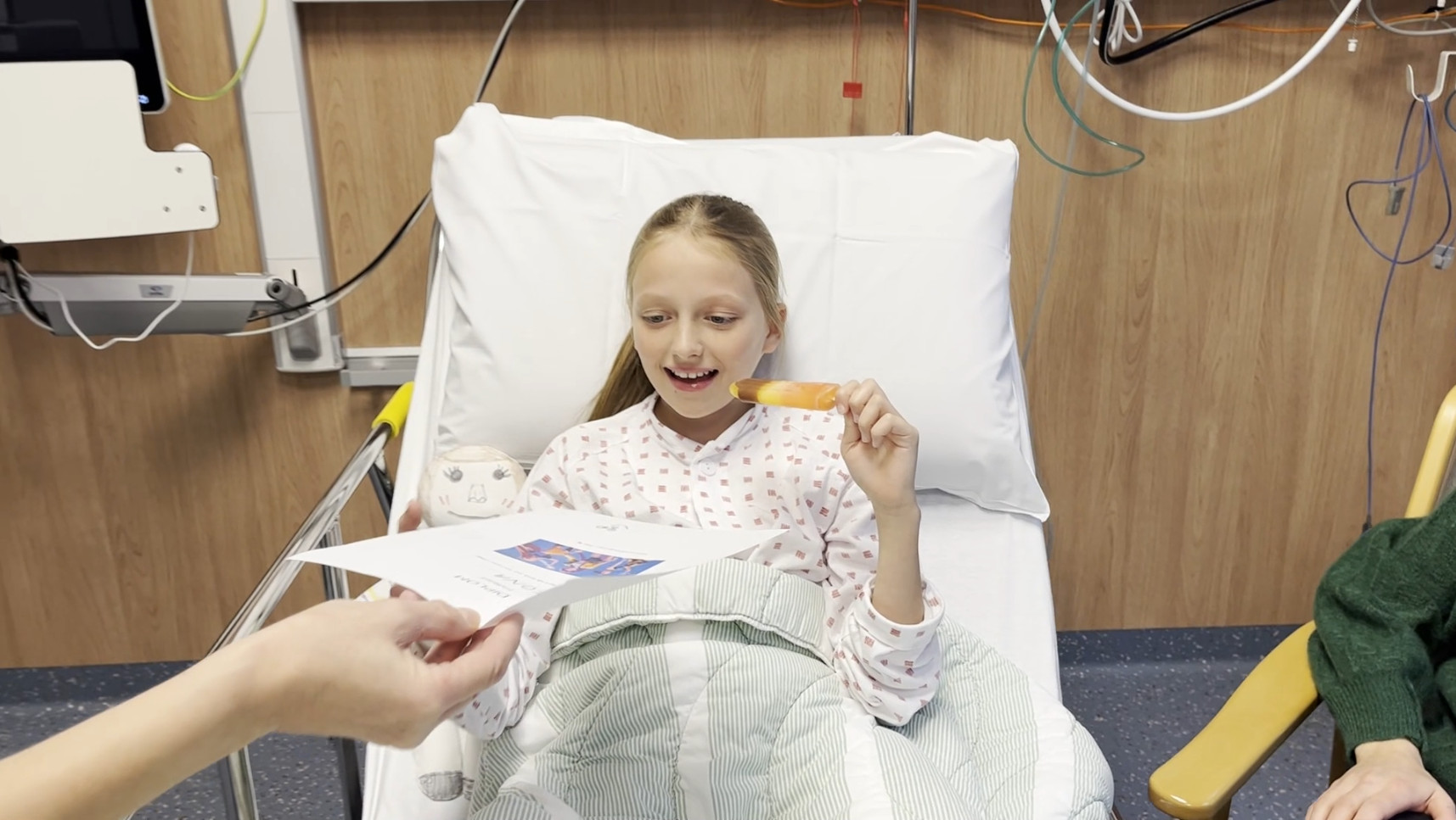 Ei smilande jente med is og diplom i sjukehusseng etter narkose. 