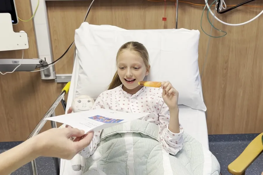 Ei smilande jente med is og diplom i sjukehusseng etter narkose.