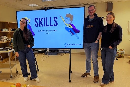 Tre tilsette ved BUP Kristiansund står ved ein stor skjem med inngangsbildet til kurset ADHD Skills.