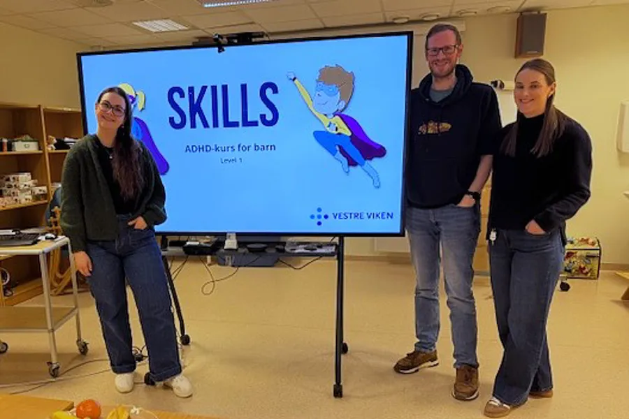 Tre tilsette ved BUP Kristiansund står ved ein stor skjem med inngangsbildet til kurset ADHD Skills.
