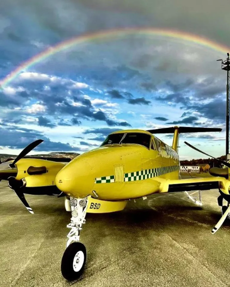 Ambulansefly på en rullebane med en regnbue i bakgrunnen