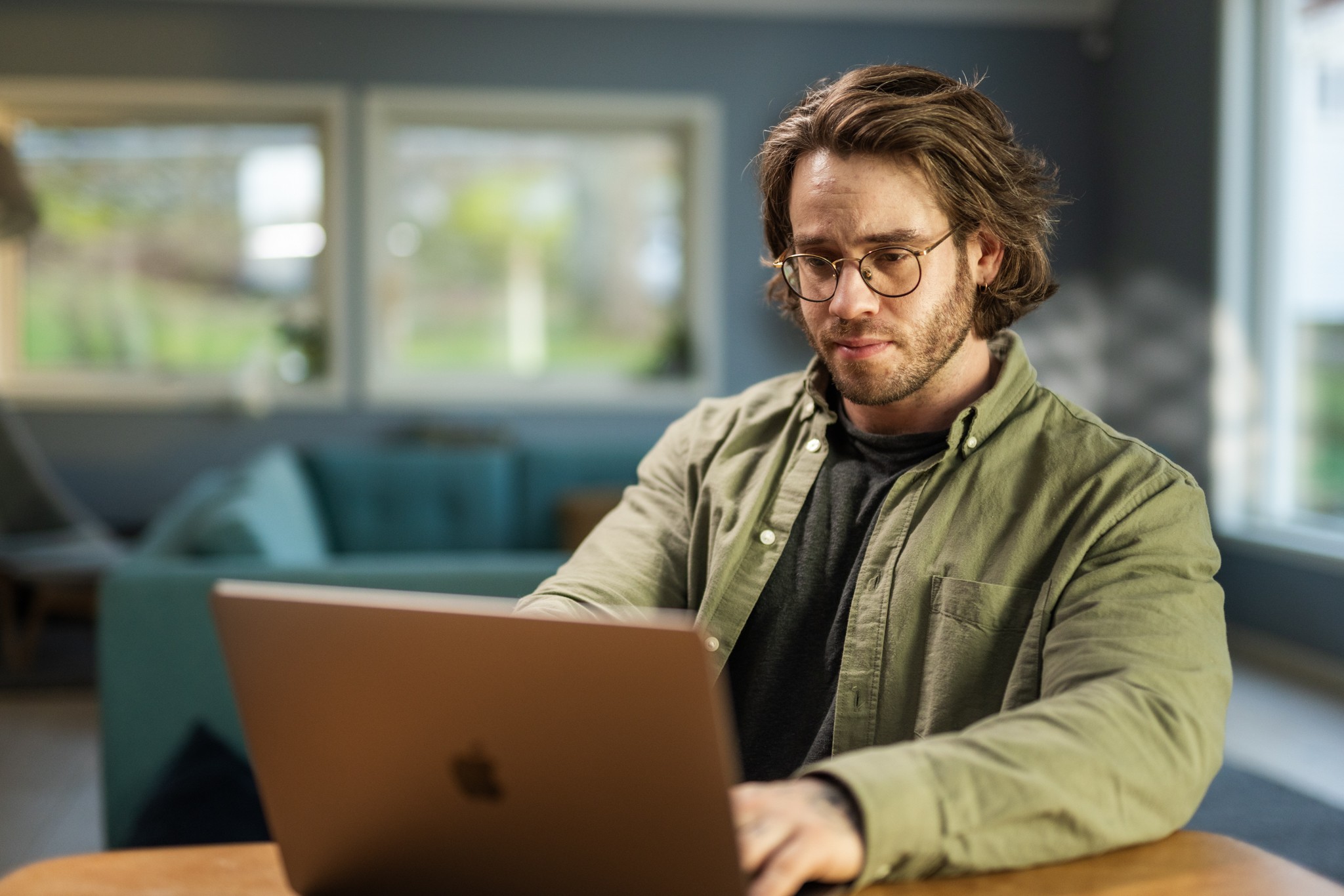 Ung mann med briller og bekymra mine i ansiktet sit ved eit bord og ser på skjermen til ein lap top.