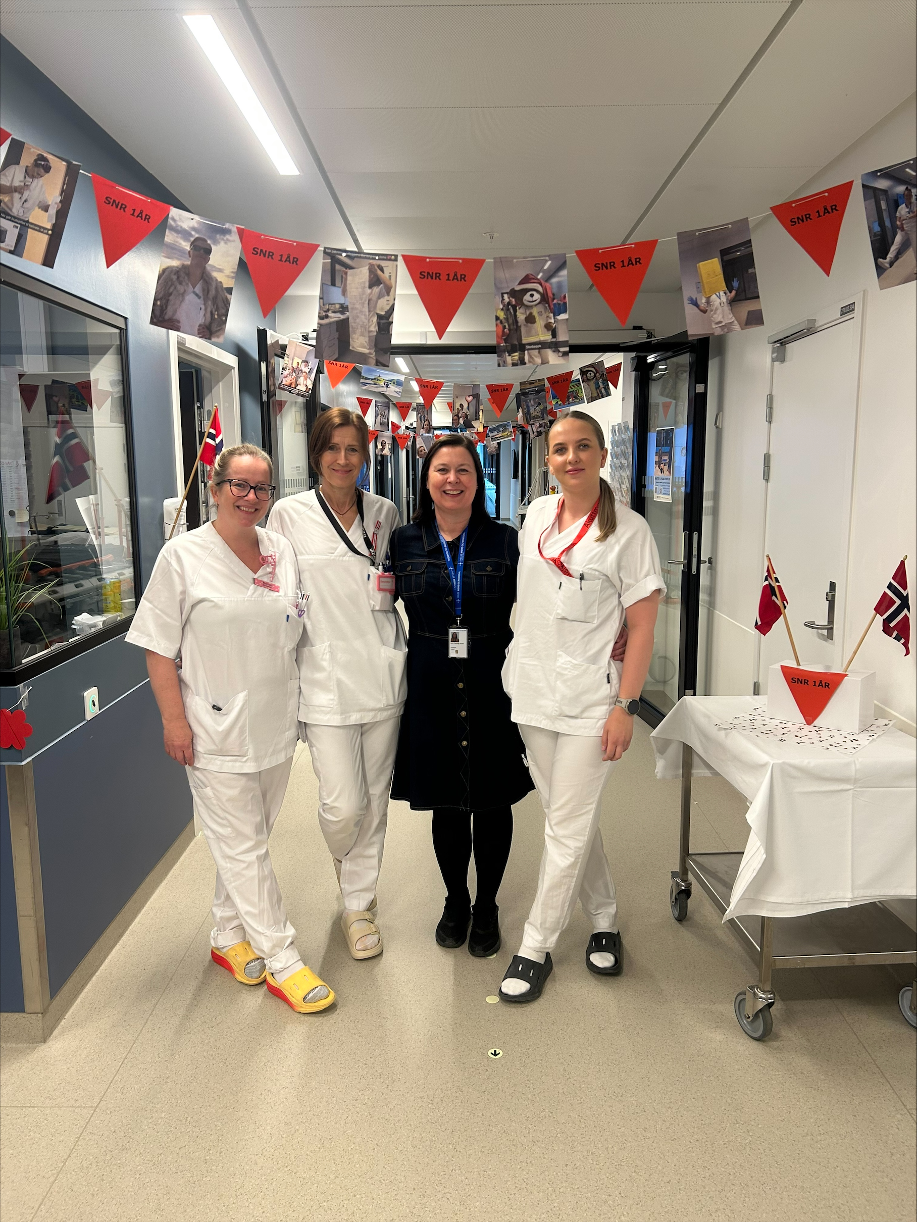 Ei gruppe tilsette i kvitt arbeidstøy står i eit rom pynta med flagg.