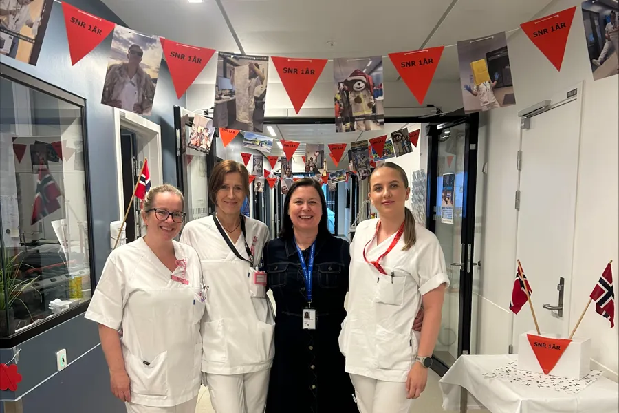 Ei gruppe tilsette i kvitt arbeidstøy står i eit rom pynta med flagg.