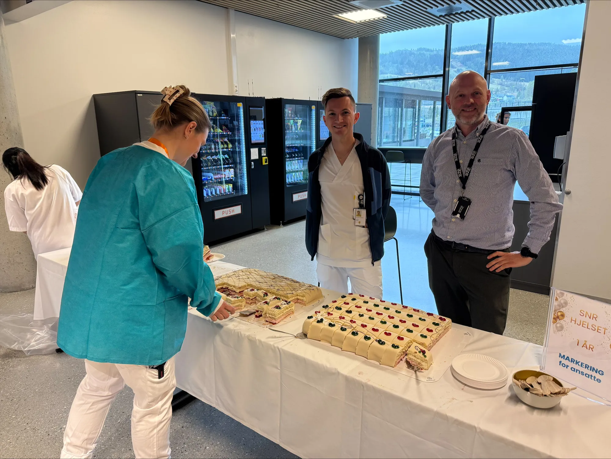 Langt bord med store marsipankaker. To tilsette smiler til kameraet