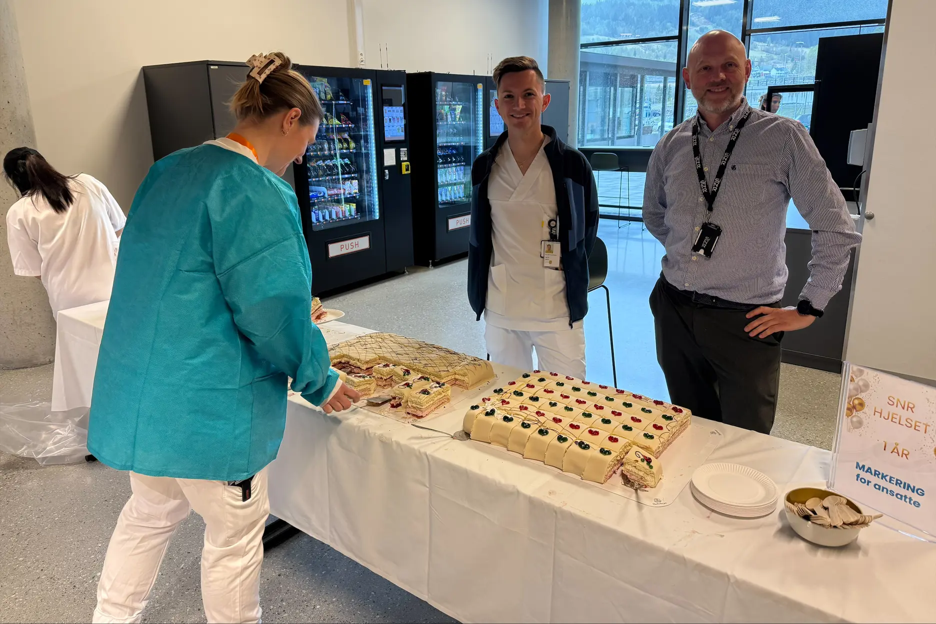 Langt bord med store marsipankaker. To tilsette smiler til kameraet