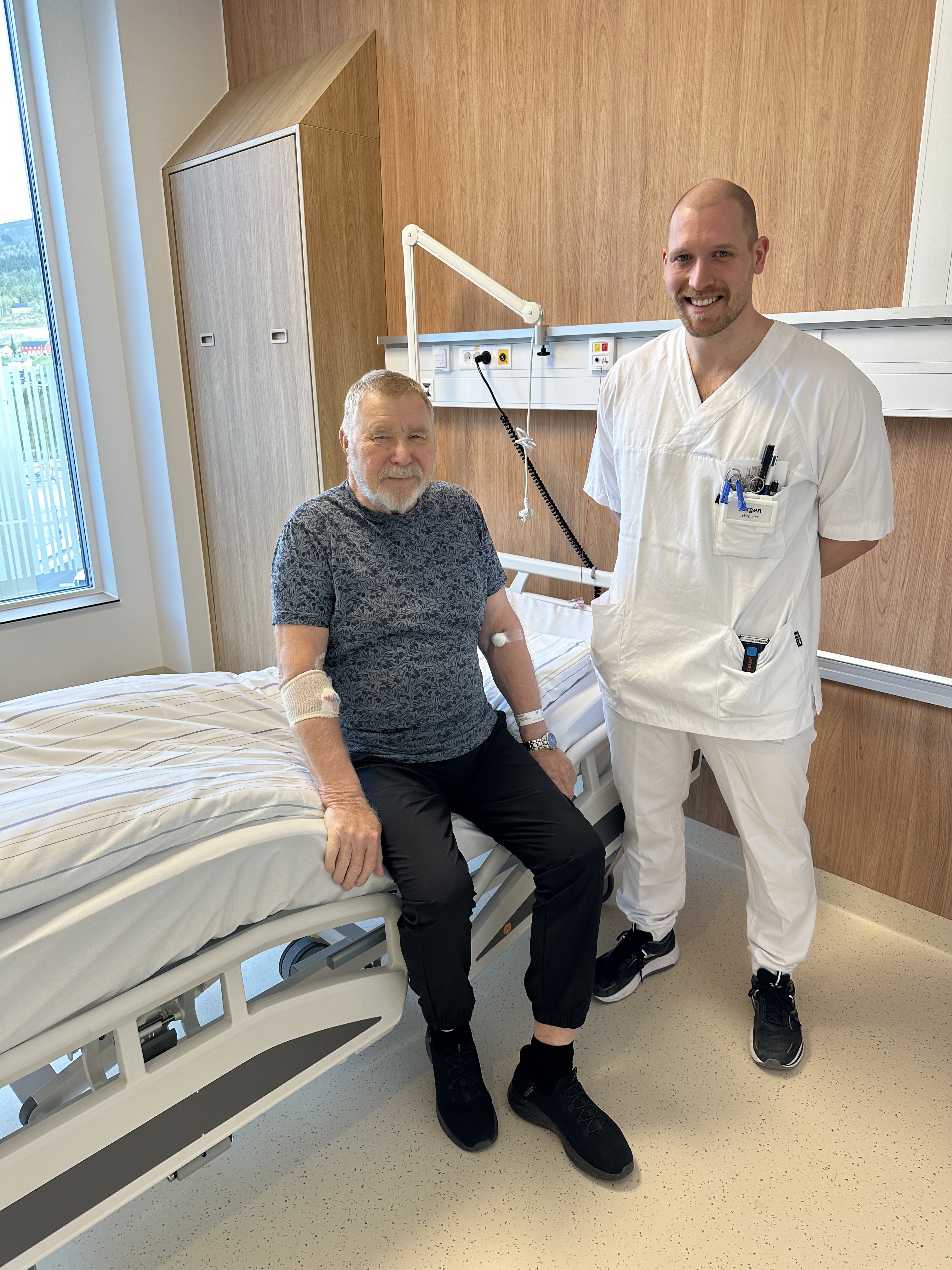 En mann som sitter på en seng med en mann stående ved siden av seg