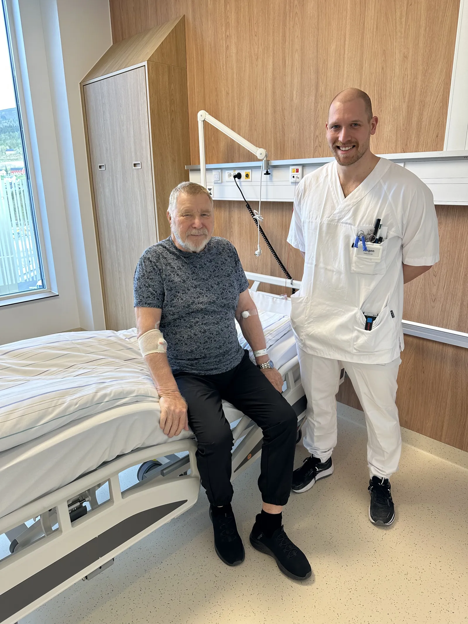 En mann som sitter på en seng med en mann stående ved siden av seg