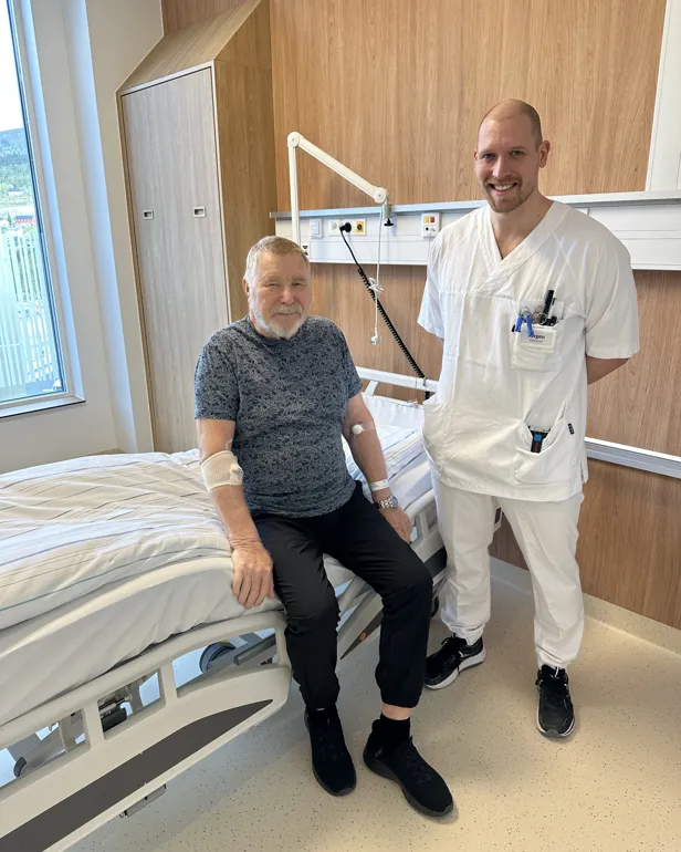 En mann som sitter på en seng med en mann stående ved siden av seg