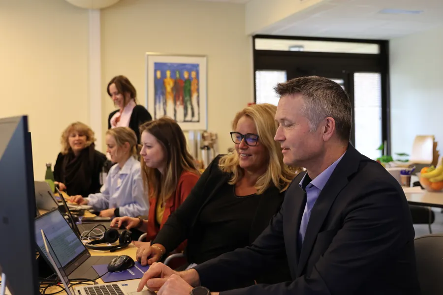 En gruppe mennesker som sitter ved et bord med datamaskiner