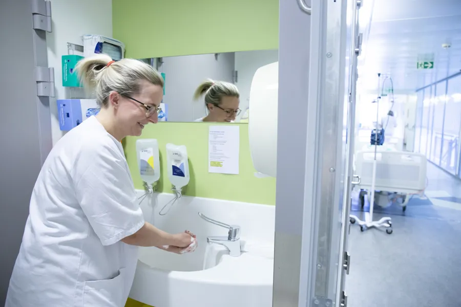 Ansatt i hvitt sykehustøy vasker hendene med skummende såpe.