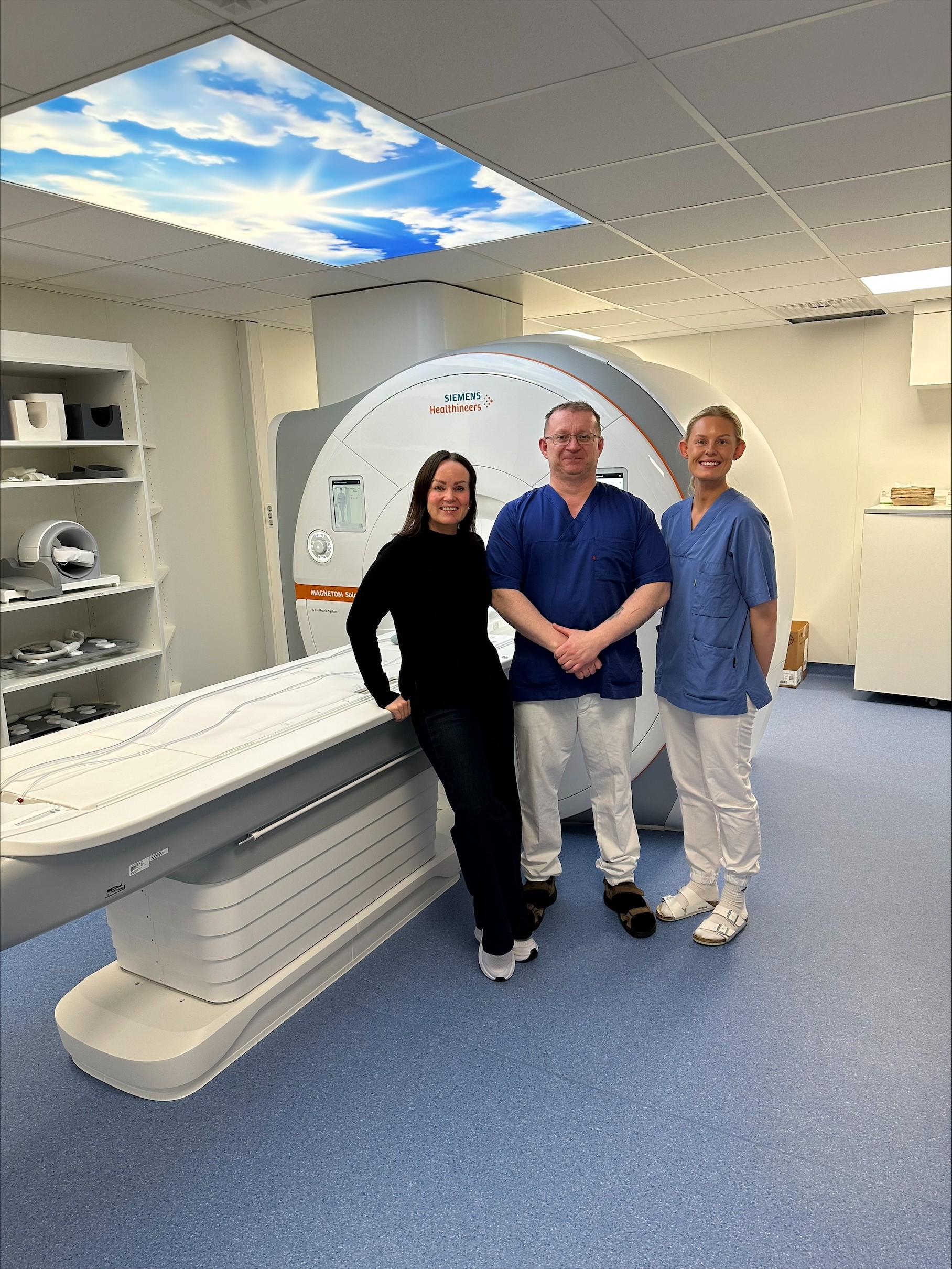 Tre ansatte som står ved siden av en MR-maskin.