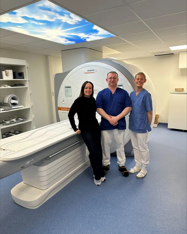 Tre ansatte som står ved siden av en MR-maskin.