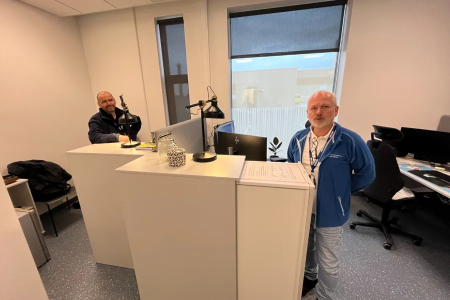 En person som står ved siden av en person som sitter ved et skrivebord