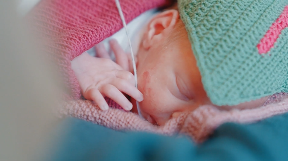 Ein prematur baby med strikka teppe og lue.