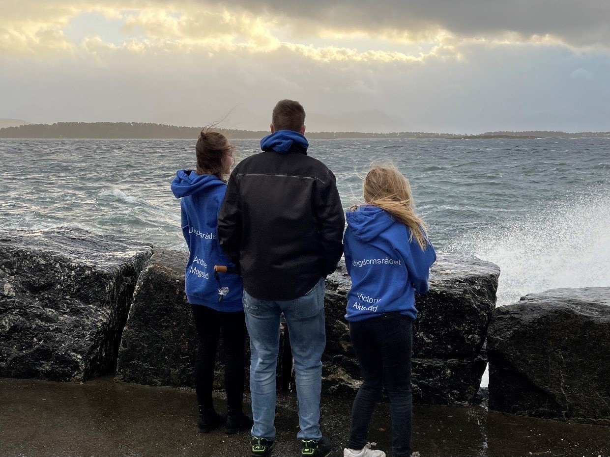 Tre ungdommar står med ryggen til og ser ut over havet.