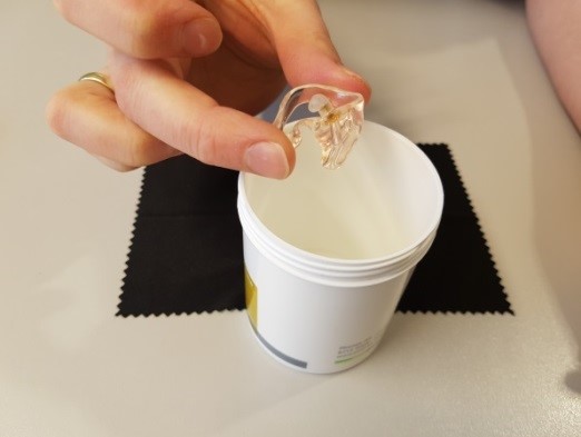 En hånd som holder en liten hvit beholder med et brunt stoff i