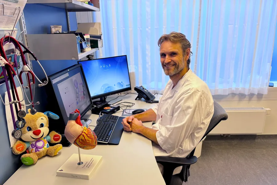 En mann som sitter ved et skrivebord med en datamaskin og et kosedyr