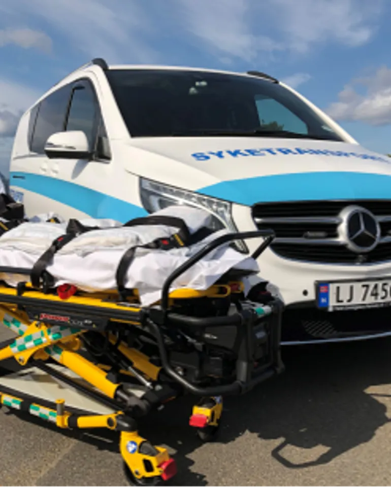 Parkert pasientreisebil med en pasientbåre foran