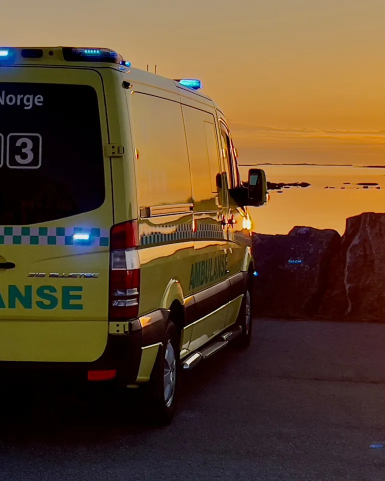 Ambulansebil som står parkert med solnedgang i bakgrunnen