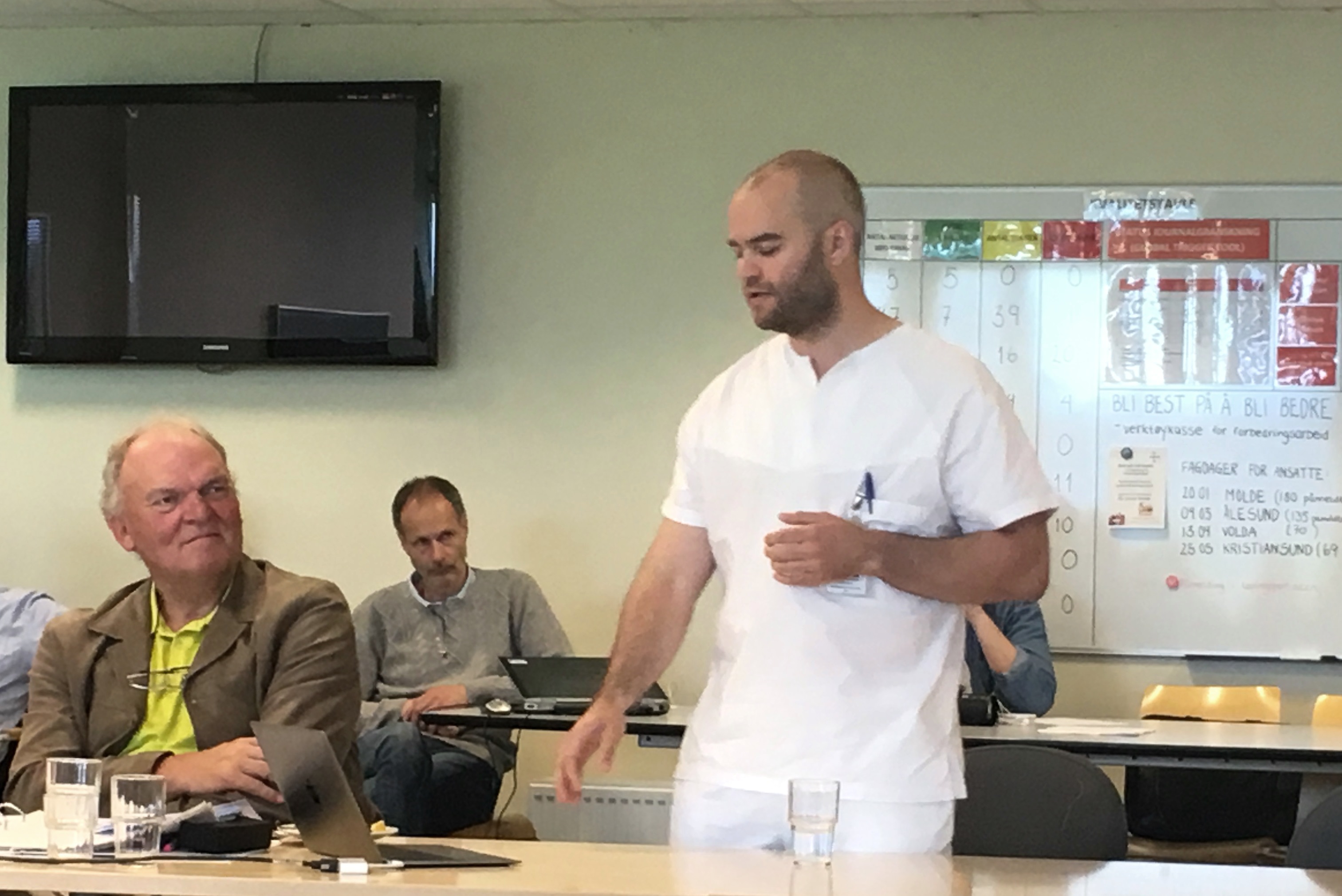 En mann som står foran et bord med andre menn som sitter ved det