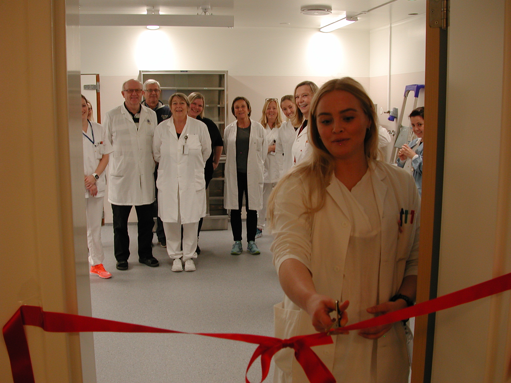 En gruppe mennesker i hvite labfrakker står i gangen