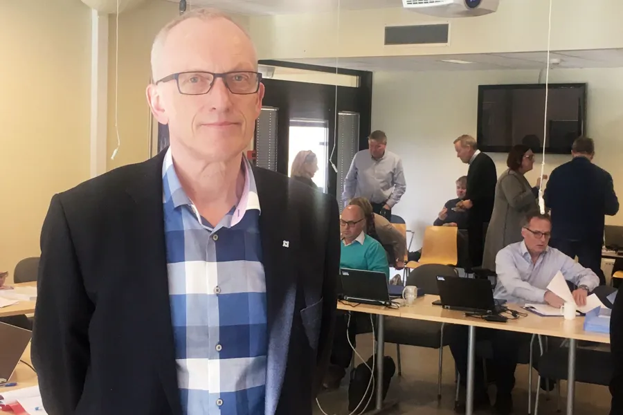 En mann som står i et rom med folk som sitter ved pulter