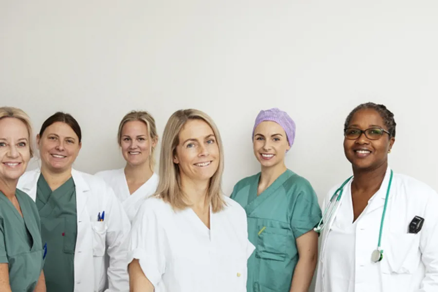 Oppstilt bilde av en gruppe smilende helsepersonell i hvitt og grønt arbeidtøy.