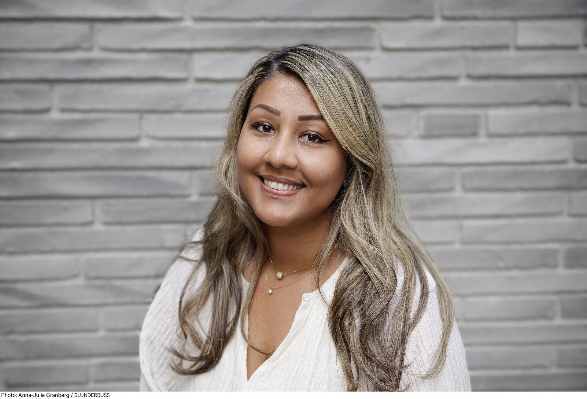 En person som smiler foran en murvegg