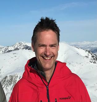 En mann som smiler foran et snødekt fjell