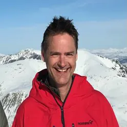 En mann som smiler foran et snødekt fjell