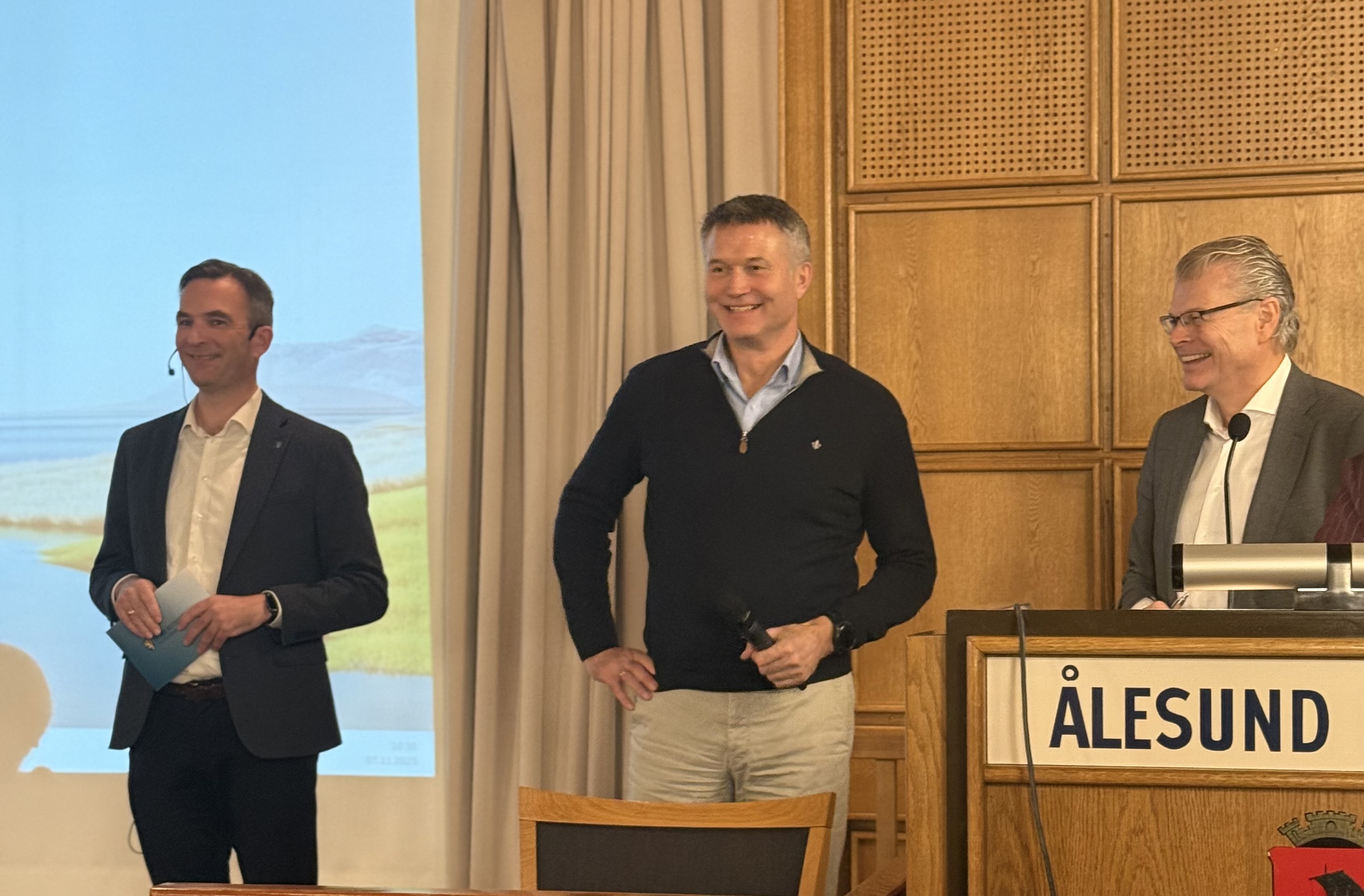 Tre menn som står foran et podium