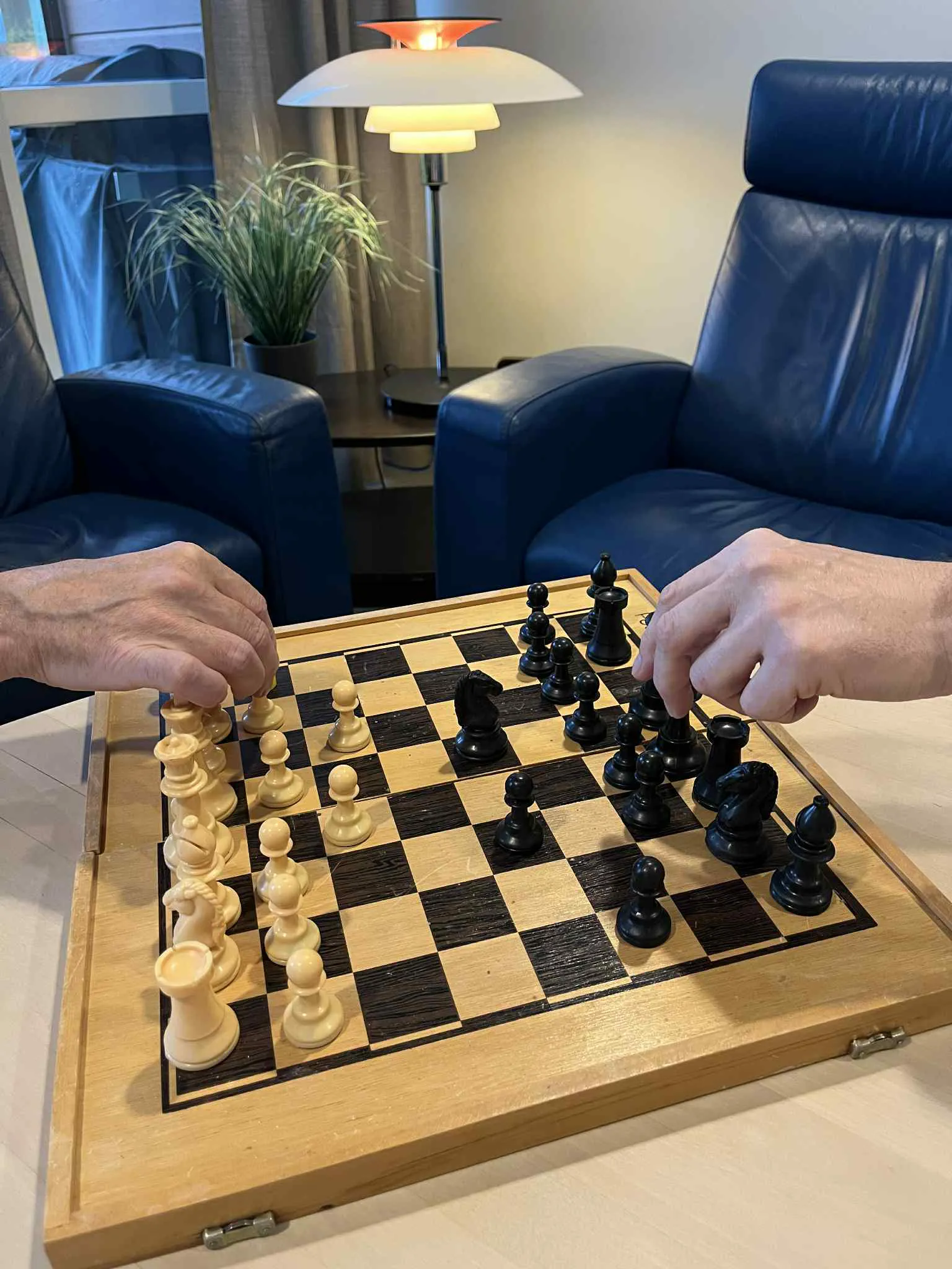 Et sjakkbrett med brikker på og to skinnstoler