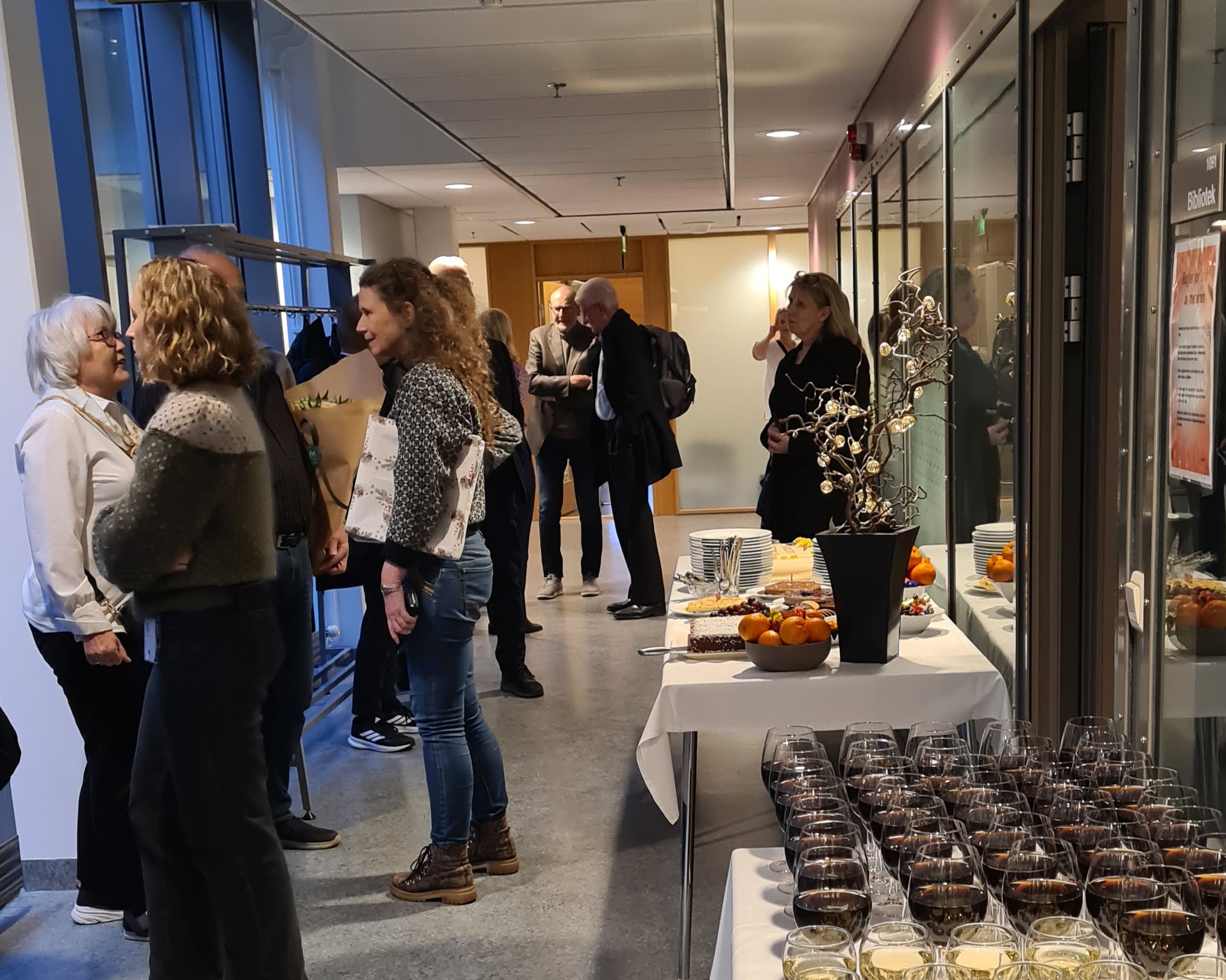 En gruppe mennesker som står i et rom med bord og stoler