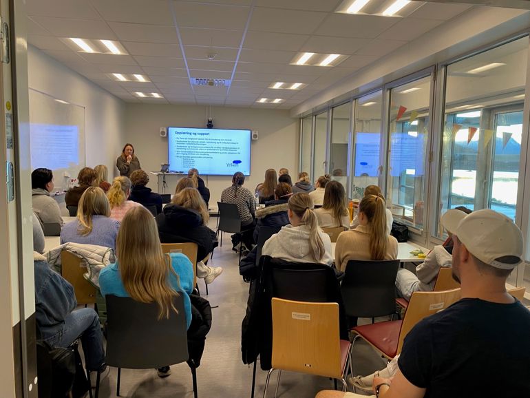 En gruppe mennesker som sitter i et rom og ser på en skjerm