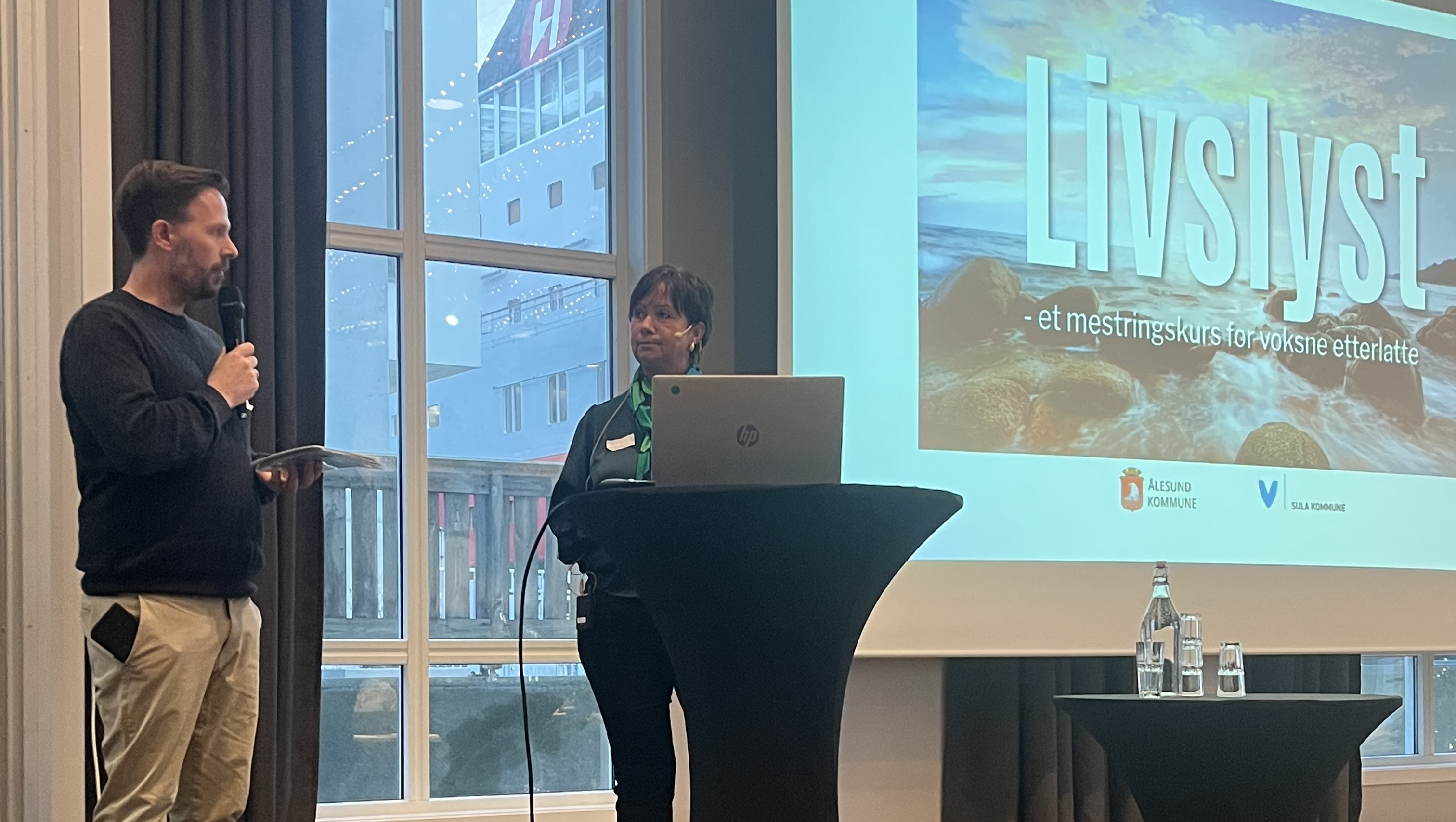 Per Magnus Hatlehol og Merete Brungot Kløvning står på scena under konferansen. I bakgrunnen ser vi presentasjon med tittel LIVSLYST.