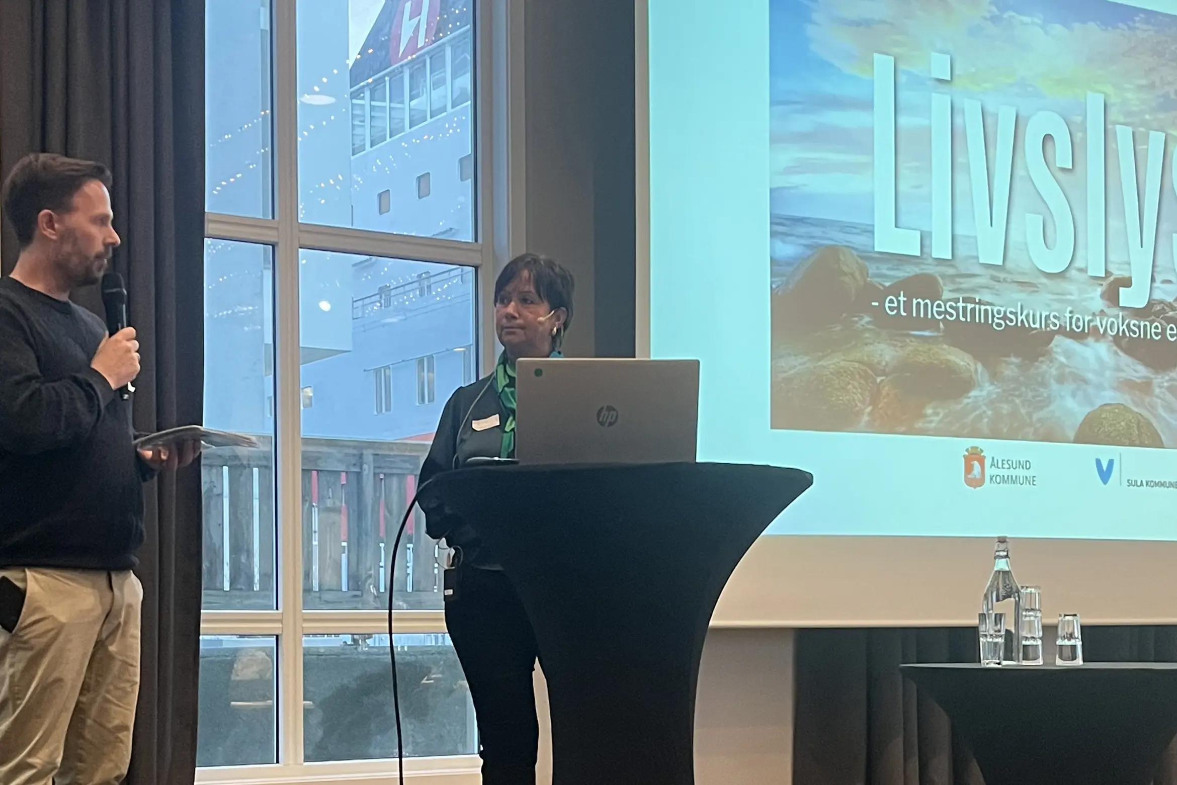 Per Magnus Hatlehol og Merete Brungot Kløvning står på scena under konferansen. I bakgrunnen ser vi presentasjon med tittel LIVSLYST.