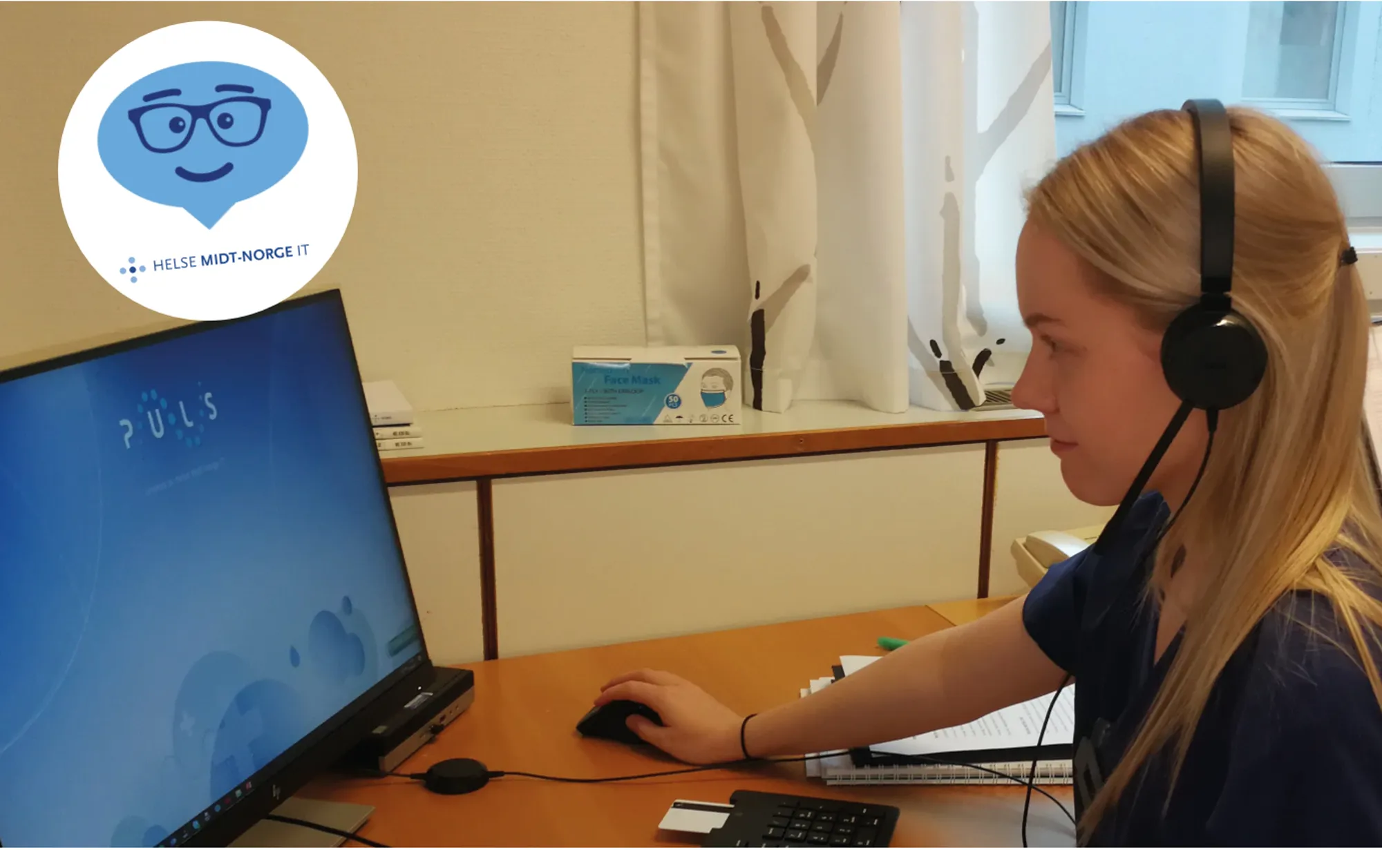 En kvinne som har på seg hodetelefoner og sitter ved et skrivebord med en datamaskin